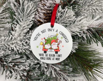 May include: A white round Christmas ornament with a red ribbon. The ornament features a cartoon illustration of two gnomes in a red truck with a Christmas tree. Text on the ornament reads: "You're not only a coworker, you're the reason I don't punch people at work."