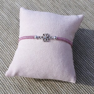 Peut inclure: Un bracelet tressé rose avec un charme de fleur argenté et des perles argentées.