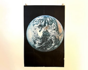 Peut inclure: Une affiche vintage représentant une image rapprochée de la Terre depuis l'espace, montrant les continents et les océans en détail. La planète est représentée sur un fond noir.