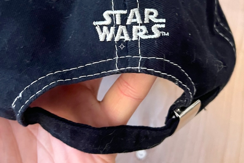 Peut inclure: Casquette de baseball noire avec un logo "STAR WARS" brod&eacute; en blanc sur le devant. La casquette a un d&eacute;tail de couture blanche autour du bord et une fermeture &agrave; boucle en m&eacute;tal argent&eacute;.