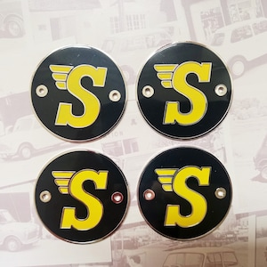 May include: Four black and yellow metal badges with the letter "S" and wings on each. The badges are round and have a shiny finish.