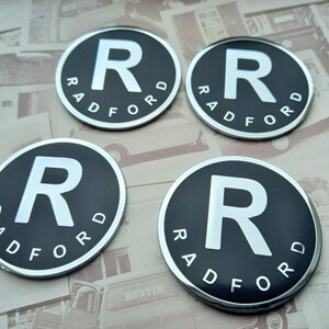 Op de afbeelding: Vier ronde badges in zwart en zilver met het woord "RADFORD" en een grote witte "R" in het midden.