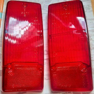 May include: A pair of rectangular, transparent red taillight lenses. Each lens features a textured lower section and vertical lines. These are vehicle taillight lenses.