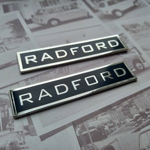 Op de afbeelding: Twee zilveren en zwarte metalen badges met het woord "RADFORD" in witte letters.