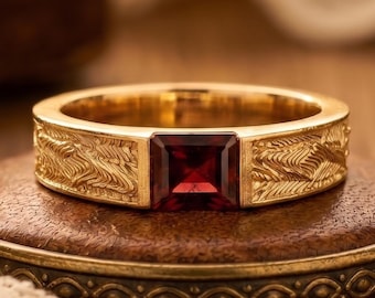 May include: A gold ring featuring a square-cut deep red gemstone set in the center. The band is crafted from yellow gold and displays a detailed, textured pattern of repeating diagonal lines etched across the surface on both sides of the stone.