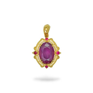 Puede incluir: Un colgante de oro con una gran piedra de rubí ovalada rodeada de pequeños acentos de rubí. El colgante tiene un diseño delicado y ornamentado.
