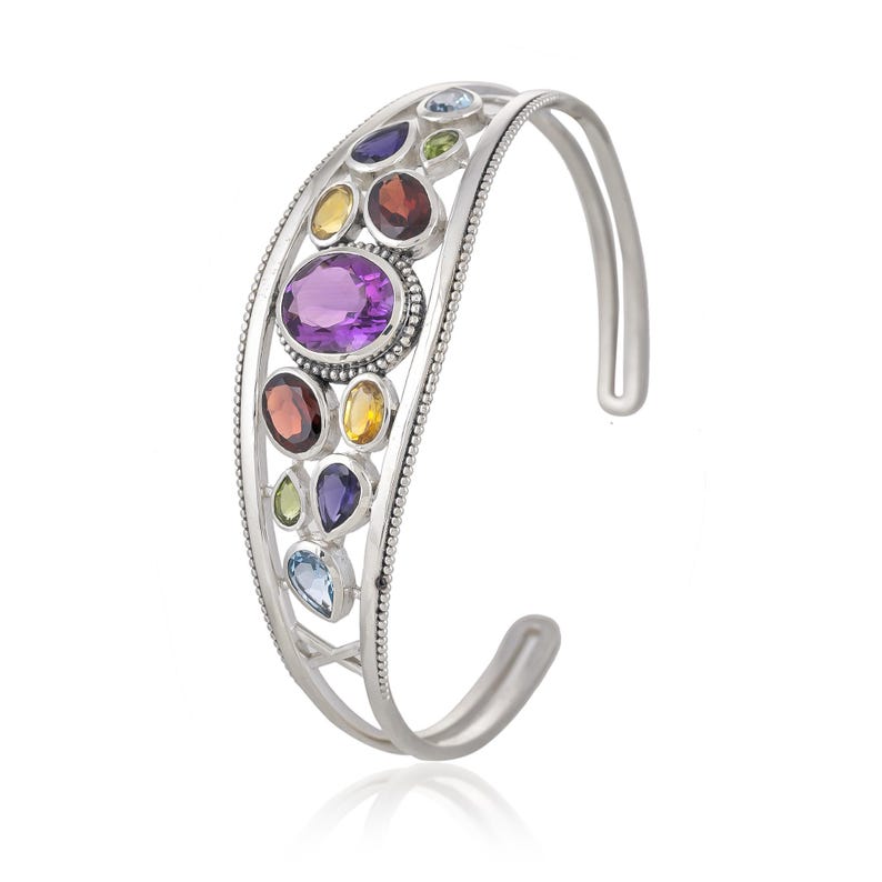 Puede incluir: Un brazalete de plata con un dise&ntilde;o delicado que presenta una variedad de piedras preciosas de colores, incluyendo amatista, granate, citrino y topacio.