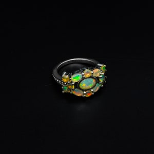 May include: A silver ring with a cluster of oval-shaped opals in shades of green, yellow, and white. The ring is set on a black background.