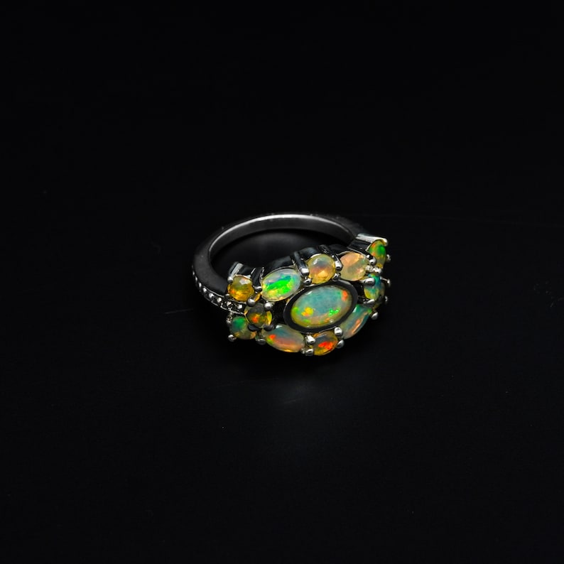 May include: A silver ring with a cluster of oval-shaped opals in shades of green, yellow, and white. The ring is set on a black background.