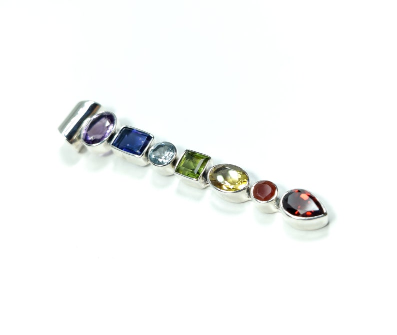 Puede incluir: Un colgante de plata con una fila de piedras preciosas de colores, incluyendo amatista, zafiro, aguamarina, peridoto, citrino, cornalina y granate.