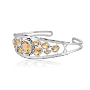 Puede incluir: Un brazalete de plata con un dise&ntilde;o delicado que presenta m&uacute;ltiples piedras preciosas de topacio facetadas. El brazalete tiene un dise&ntilde;o ligeramente abierto, lo que le permite ajustarse a diferentes tama&ntilde;os de mu&ntilde;eca.