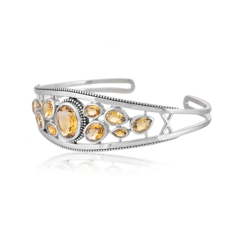 Puede incluir: Un brazalete de plata con un dise&ntilde;o delicado que presenta m&uacute;ltiples piedras preciosas de topacio facetadas. El brazalete tiene un dise&ntilde;o ligeramente abierto, lo que le permite ajustarse a diferentes tama&ntilde;os de mu&ntilde;eca.
