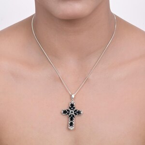 May include: A silver chain necklace with a black gemstone cross pendant. The cross is adorned with smaller black gemstones.