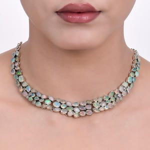 May include: A silver necklace with a multi-layered design featuring iridescent opal stones. The necklace is made of silver and has a delicate, feminine look.