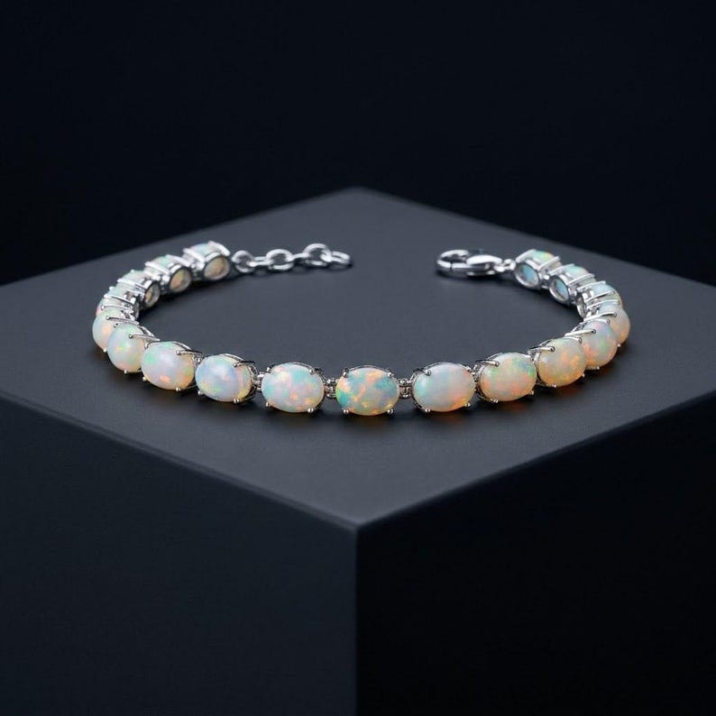 May include: A silver-toned bracelet featuring a series of oval-shaped, iridescent opals set in individual metal prongs. The bracelet includes a secure lobster claw clasp and a short extender chain with small circular links for adjustable sizing.