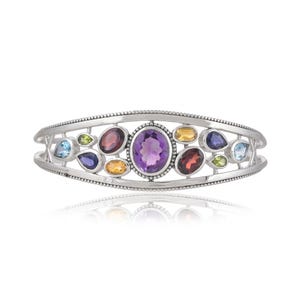 Puede incluir: Un brazalete de plata con un dise&ntilde;o delicado que presenta una variedad de piedras preciosas de colores, incluyendo amatista, granate, peridoto y topacio.