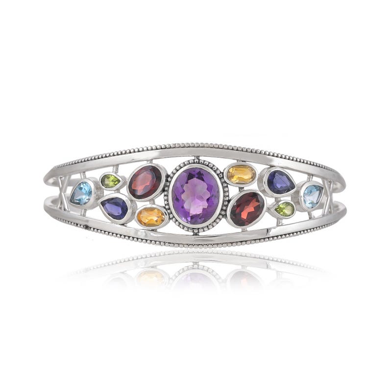 Puede incluir: Un brazalete de plata con un dise&ntilde;o delicado que presenta una variedad de piedras preciosas de colores, incluyendo amatista, granate, peridoto y topacio.