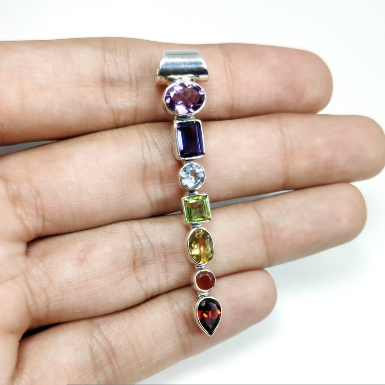 Puede incluir: Un colgante de plata con siete piedras preciosas en una secuencia de colores arco&iacute;ris. Las piedras son amatista, zafiro, aguamarina, peridoto, citrino, cornalina y granate.