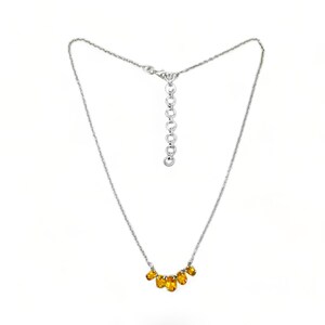 May include: A silver chain necklace with a delicate row of oval-shaped amber gemstones.