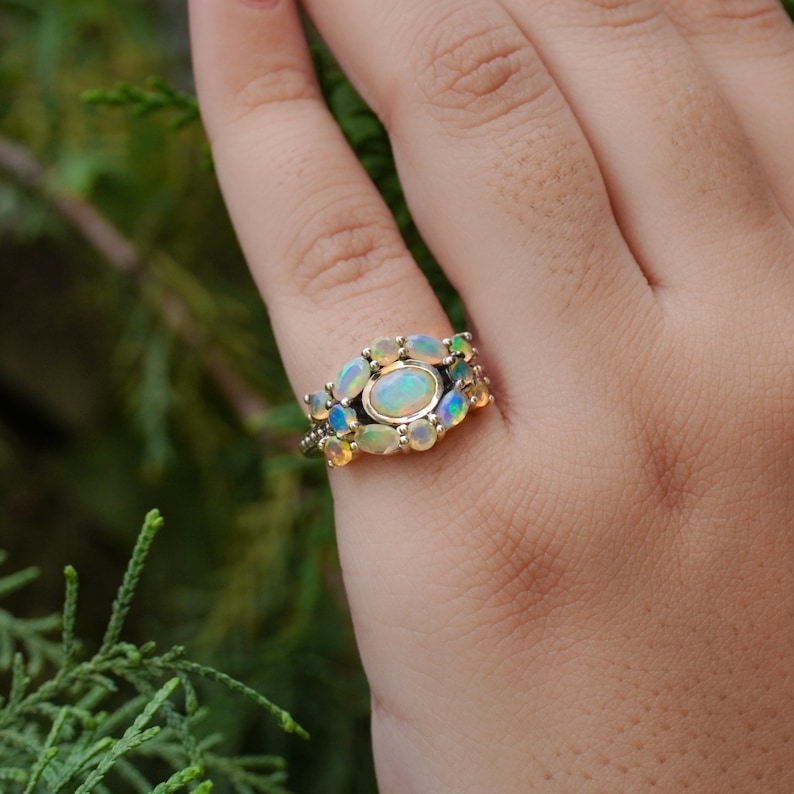 May include: A gold ring with a large oval opal surrounded by smaller opals. The ring is set in a silver band.