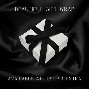 May include: A square white gift box tied with a black ribbon bow. The text BEAUTIFUL GIFT WRAP is printed at the top and AVAILABLE AT JUST $3 EXTRA is printed at the bottom of the image against a dark, draped fabric background.