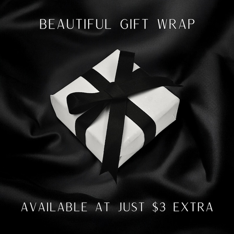 May include: A square white gift box tied with a black ribbon bow. The text BEAUTIFUL GIFT WRAP is printed at the top and AVAILABLE AT JUST $3 EXTRA is printed at the bottom of the image against a dark, draped fabric background.