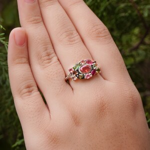 K&ouml;nnte beinhalten: Ein Ring mit einem Cluster aus rosa, gr&uuml;nen und schwarzen Edelsteinen, die in einer silbernen Fassung sitzen.