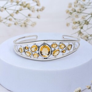 Puede incluir: Un brazalete de plata con un dise&ntilde;o delicado que presenta m&uacute;ltiples piedras de citrino ovaladas y en forma de l&aacute;grima. El brazalete tiene un acabado pulido y un borde con cuentas.