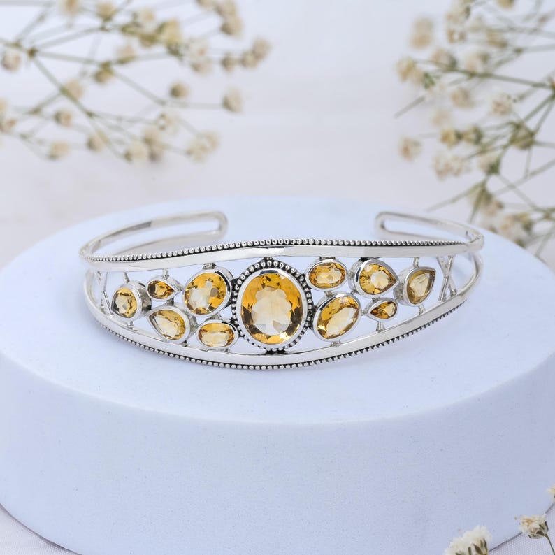 Puede incluir: Un brazalete de plata con un dise&ntilde;o delicado que presenta m&uacute;ltiples piedras de citrino ovaladas y en forma de l&aacute;grima. El brazalete tiene un acabado pulido y un borde con cuentas.