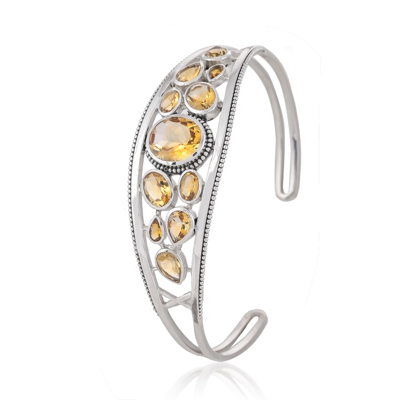 Puede incluir: Pulsera de brazalete de plata con un dise&ntilde;o curvo que presenta un grupo de piedras preciosas de topacio facetadas.