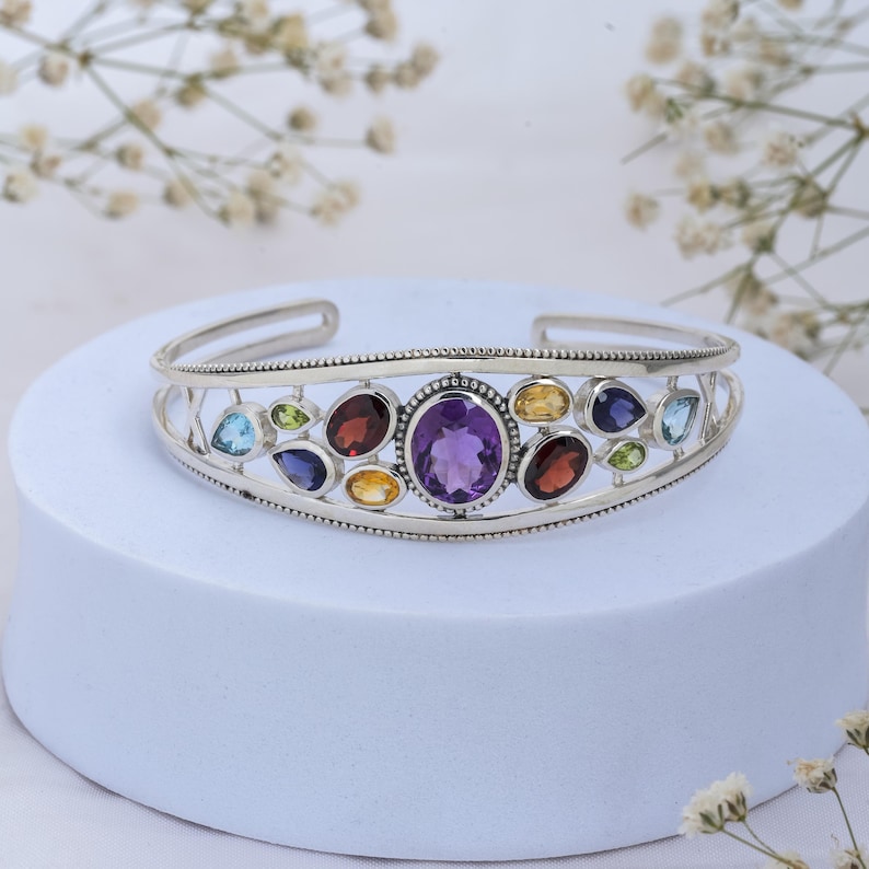 Puede incluir: Un brazalete de plata con un dise&ntilde;o delicado que presenta una variedad de piedras preciosas de colores, incluyendo amatista, granate, peridoto y citrino.