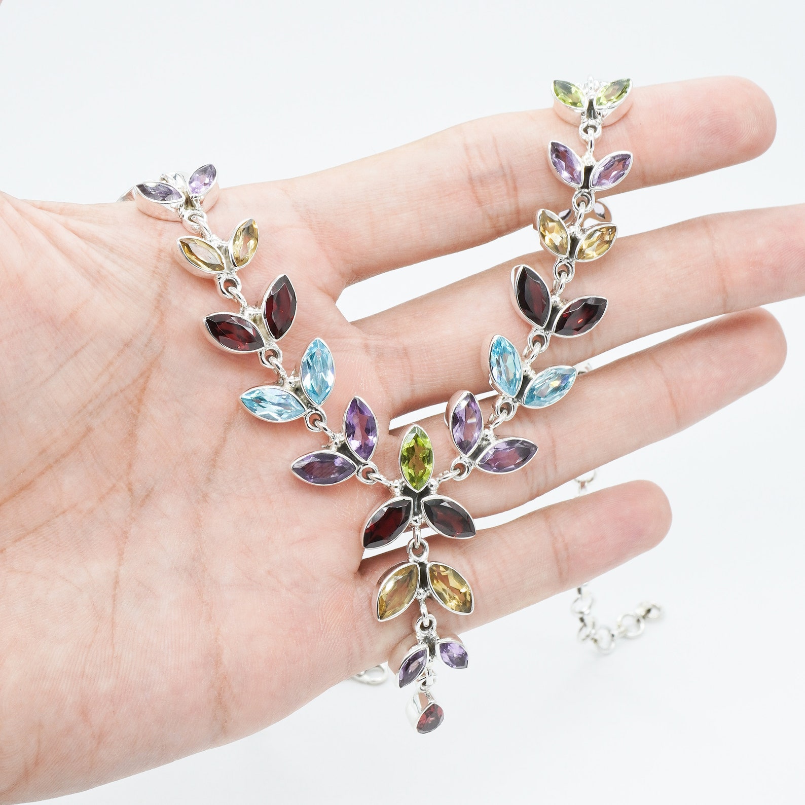 Sterling silver leaf necklace with garnet, amethyst, moonstone, and blue topaz stones held in a hand.