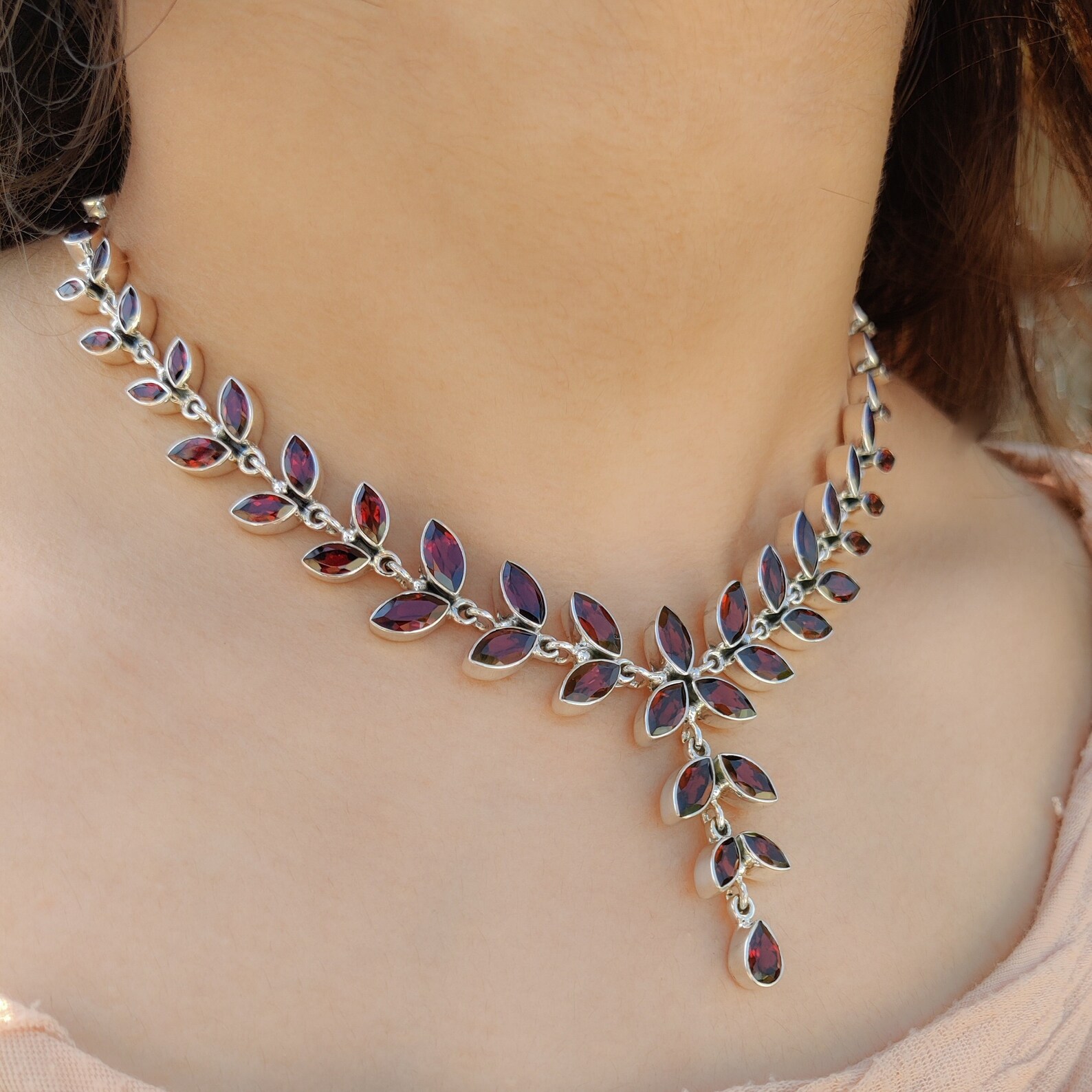 Sterling silver necklace with natural garnet leaf-shaped stones worn on a woman's neck.