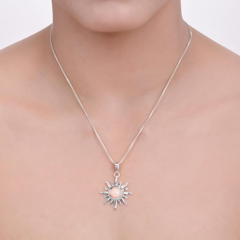 Op de afbeelding: Een zilveren ketting met een delicate ketting en een hanger in de vorm van een zon met een roze opaal-steen in het midden.