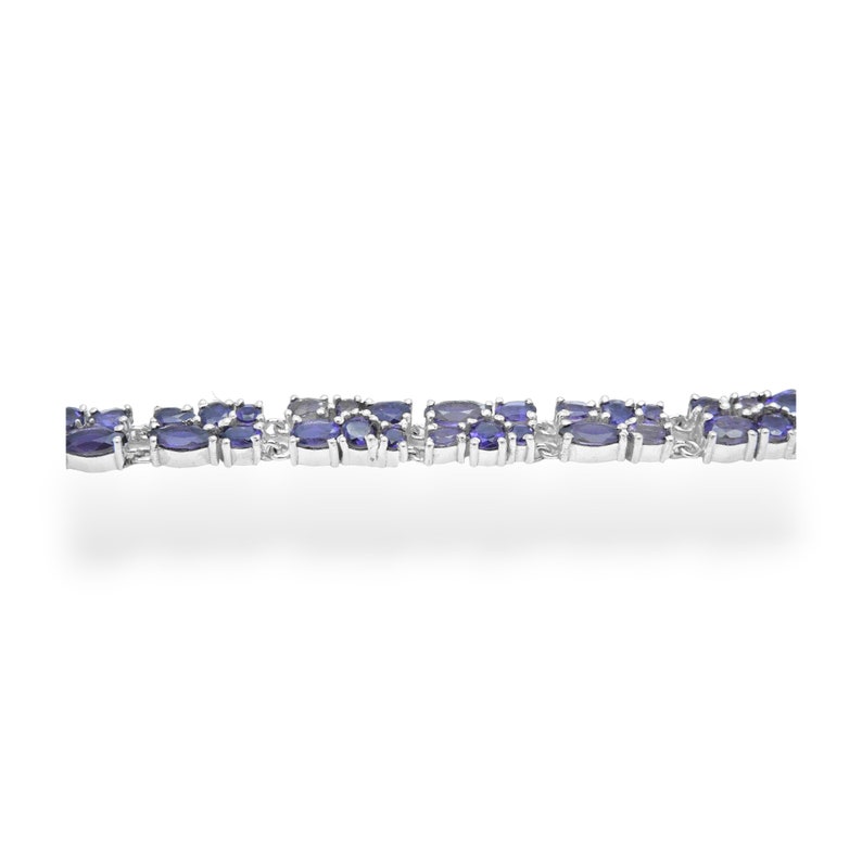 May include: A silver bracelet featuring a series of oval-shaped, deep blue gemstones. The gemstones are set closely together, creating a continuous pattern. The bracelet is displayed against a white background, highlighting the jewelry's design.