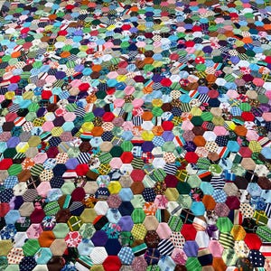 May include: A patchwork quilt made from numerous fabric hexagons in a variety of colours and patterns. The quilt displays a vibrant mix of hues, including red, blue, green, and purple. The geometric design creates a visually appealing textile.