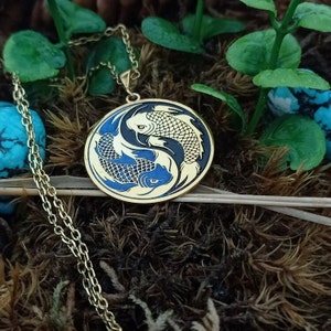 May include: A gold necklace with a round pendant featuring two black and blue koi fish swimming in a yin yang design.