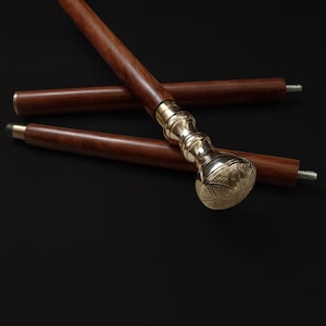 Peut inclure: Une canne en bois avec une poignée en laiton. La canne est marron foncé avec une poignée en laiton décorative. La poignée a un design orné. La canne est posée sur une surface noire.