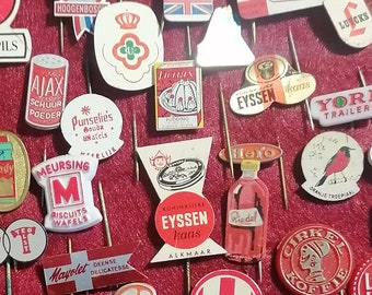 Op de afbeelding: Een verzameling vintage emaille pins met verschillende logo's en ontwerpen. De pins worden getoond op een rode vilt achtergrond en bevatten merken zoals "Opti lon", "Meenk", "Kolibiri Koffie", "Velpon", "Unx", "Radion Rekord" en "Slank met Siks".