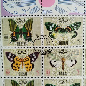 May include: A sheet of postage stamps from Dubai featuring colorful butterfly illustrations. Each stamp displays a different butterfly species with intricate wing patterns, set against a patterned background. The stamps are marked with the value of 60 Dirham.