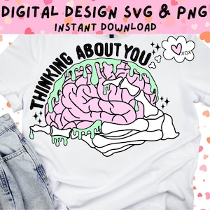 May include: A white t-shirt with a black and pink brain graphic with green slime dripping from it. The text "Thinking About You" is written around the brain. A thought bubble with a heart and the text "xox" is in the top right corner.