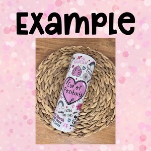 Peut inclure: Un gobelet en acier inoxydable blanc avec un c&oelig;ur rose et le texte "Cup of Positivity" entour&eacute; de gribouillis color&eacute;s et de phrases inspirantes comme "Love Yourself" et "I Can Do This".