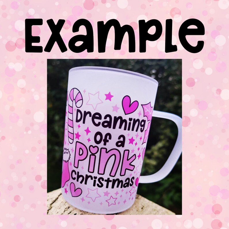 K&ouml;nnte beinhalten: Eine wei&szlig;e Keramiktasse mit einem rosafarbenen Design, auf dem "dreaming of a pink christmas" steht. Das Design enth&auml;lt Zuckerstangen, Sterne und Herzen.
