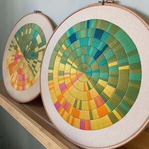 K&ouml;nnte beinhalten: Zwei runde Stickrahmen mit bunten geometrischen Mustern. Die Muster bestehen aus verschiedenen Gr&uuml;nt&ouml;nen, Gelb, Orange und Rosa.