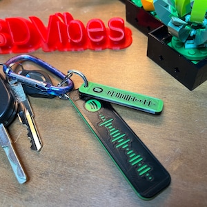 May include: A black and green key chain with a Spotify logo and a barcode design. The keychain is attached to a set of keys, including a car key with a Ford logo.