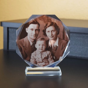 May include: A crystal paperweight with a sepia-toned photo of a family. The photo shows a man, a woman, and a child. The man is wearing a suit and tie, the woman is wearing a dress, and the child is wearing a patterned shirt. The paperweight has a clear base.