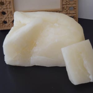 May include: Two blocks of white, solid, unscented, natural beeswax. The blocks are irregular in shape and have a smooth, slightly textured surface.