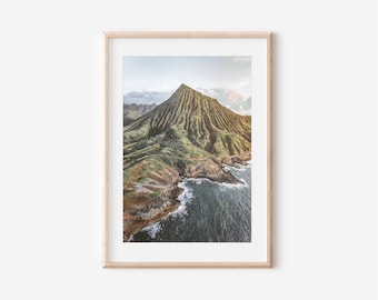 May include: An aerial view of a green mountain with a rocky coastline and blue ocean water.
