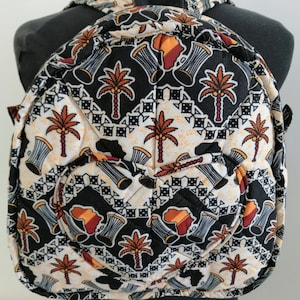 Könnte beinhalten: Ein gesteppter Rucksack in Schwarz und Weiß mit einem Muster aus Trommeln und Palmen. Der Rucksack hat eine herzförmige Tasche auf der Vorderseite.