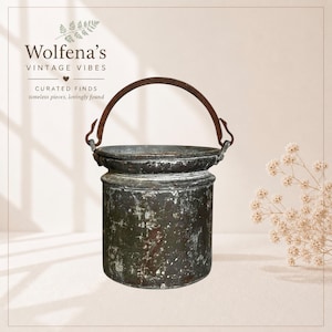 May include: A vintage metal bucket with a curved handle. The bucket has a weathered, aged appearance with a dark, mottled finish. The text "Wolfena's Vintage Vibes" is at the top, with "Curated Finds, timeless pieces, lovingly found" below.